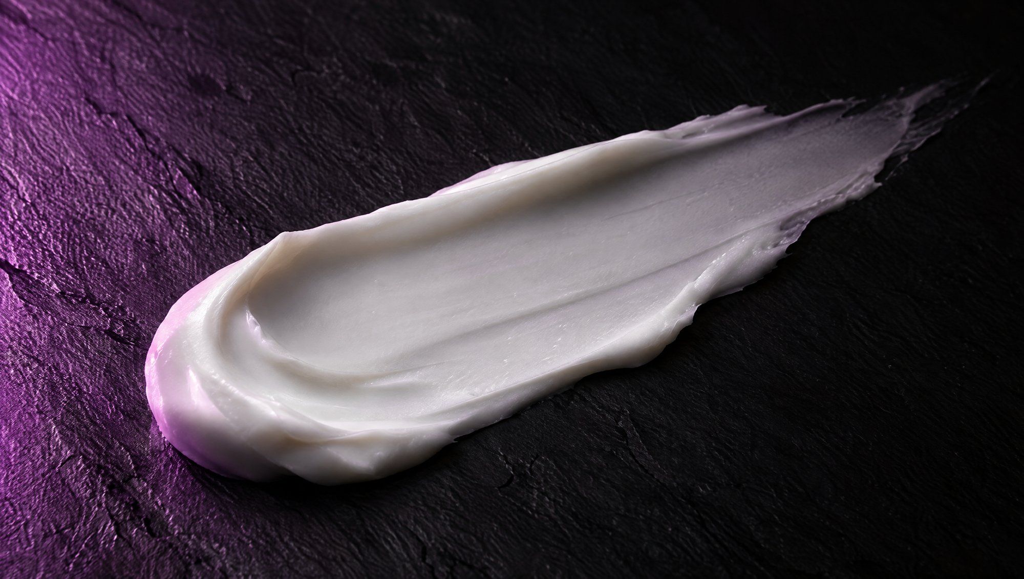 A single swatch of white cream spread across dark slate, grazed by plum light from the side.