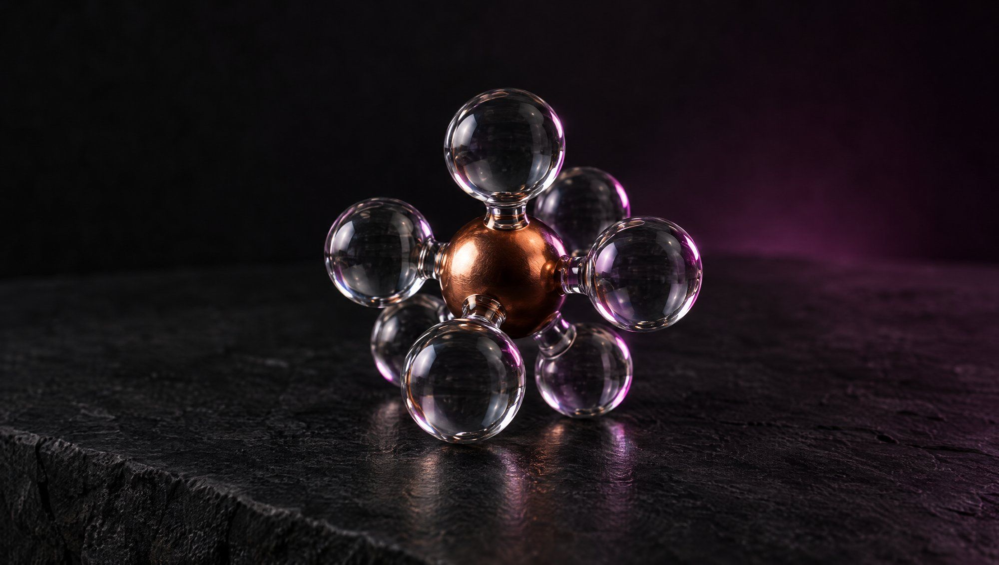 A small molecular model of clear glass spheres around one copper-colored sphere, on dark stone, rimmed in plum light.